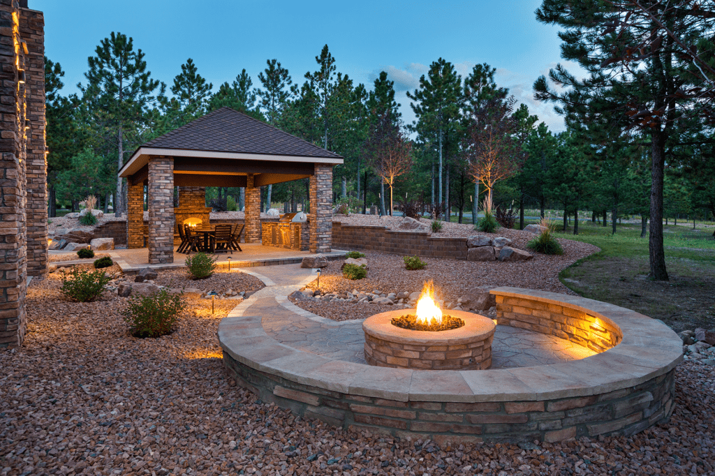 Outdoor building with living quarters in background and fire pit in the foreground with seating around the file.